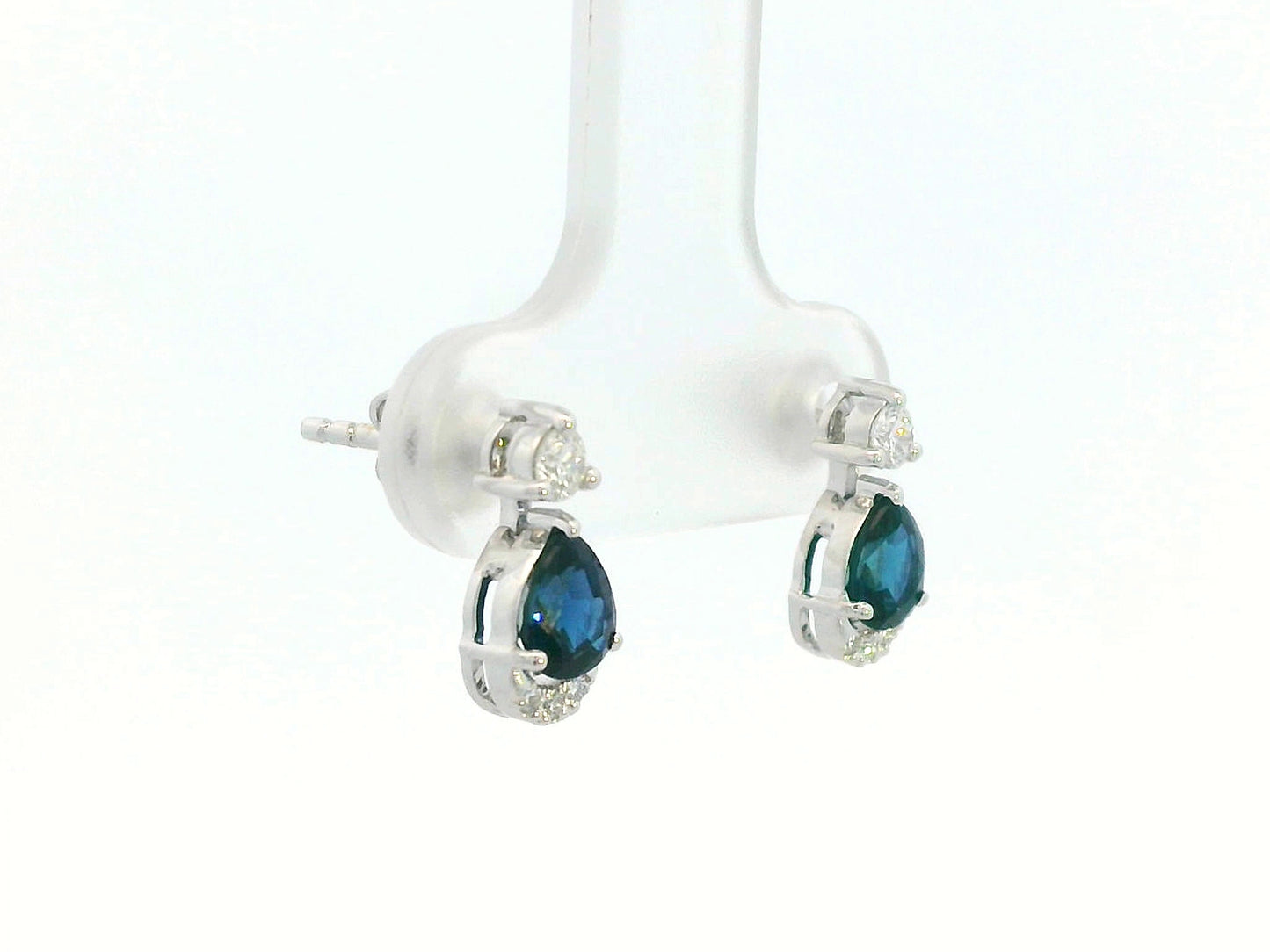 18K white gold drop earrings featuring 0.90ct pear-cut blue sapphires suspended beneath round brilliant diamonds with 0.15ct pavé diamond accent arc.
