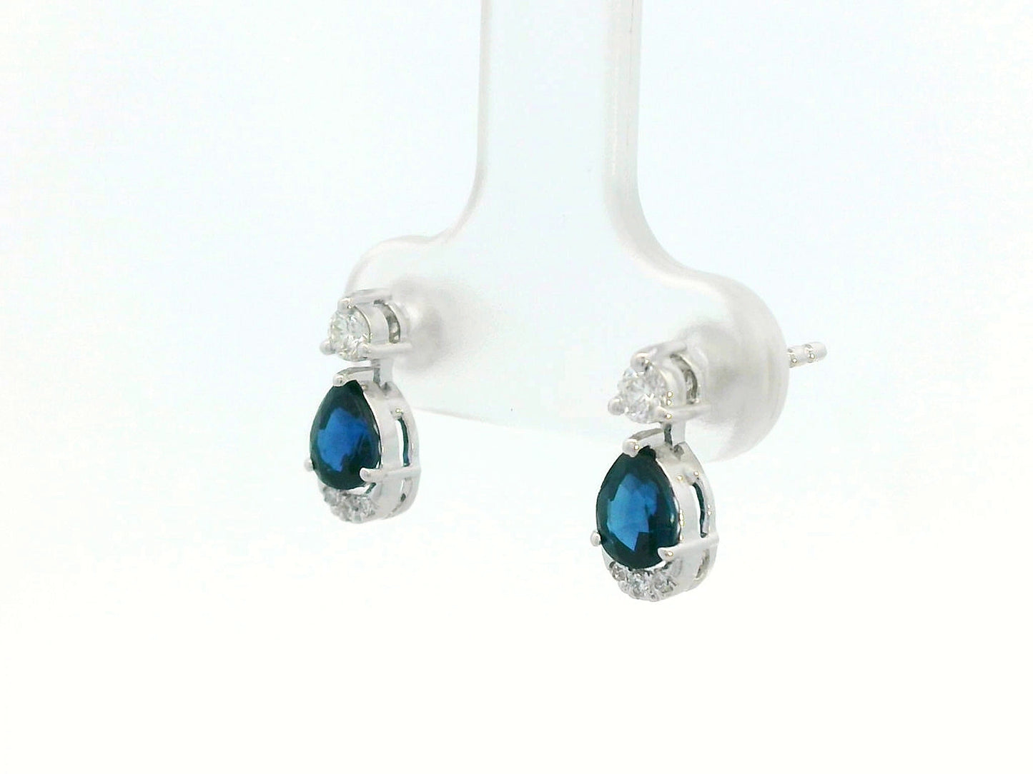18K white gold drop earrings featuring 0.90ct pear-cut blue sapphires suspended beneath round brilliant diamonds with 0.15ct pavé diamond accent arc.