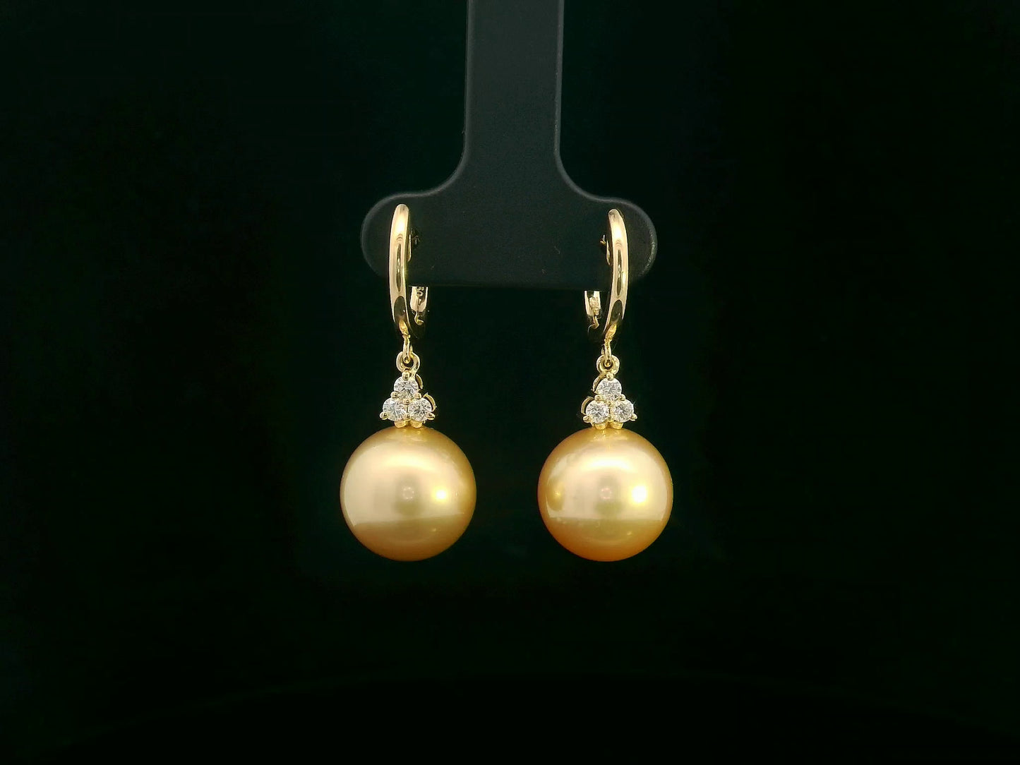 18k yellow gold South Sea pearl earrings featuring golden pearls suspended from hoops with diamond pyramid clusters above each pearl.