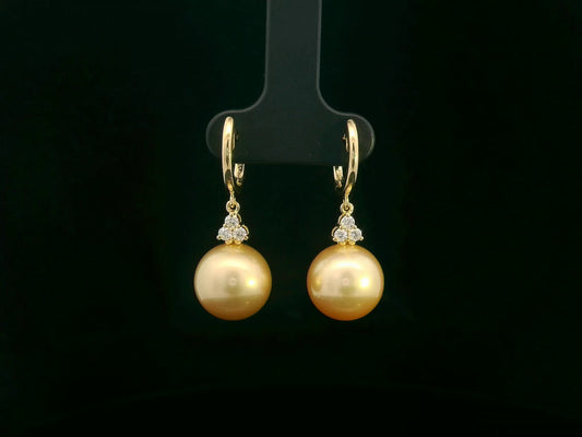 18k yellow gold South Sea pearl earrings featuring golden pearls suspended from hoops with diamond pyramid clusters above each pearl.