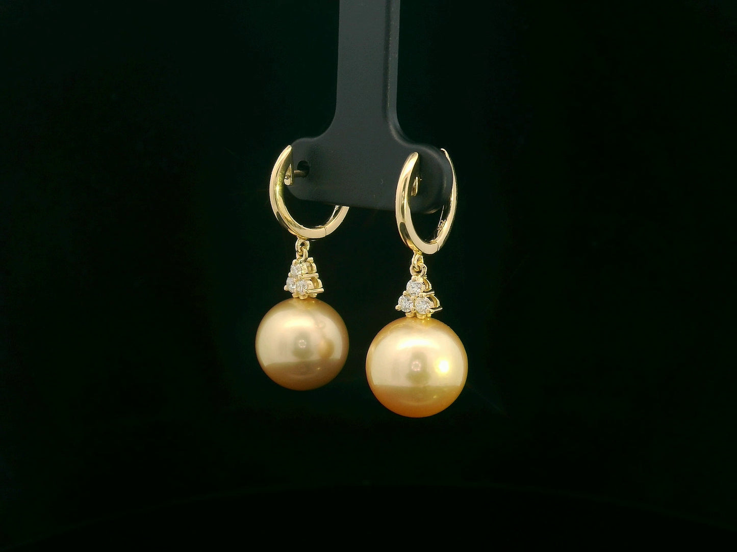 18k yellow gold South Sea pearl earrings featuring golden pearls suspended from hoops with diamond pyramid clusters above each pearl.