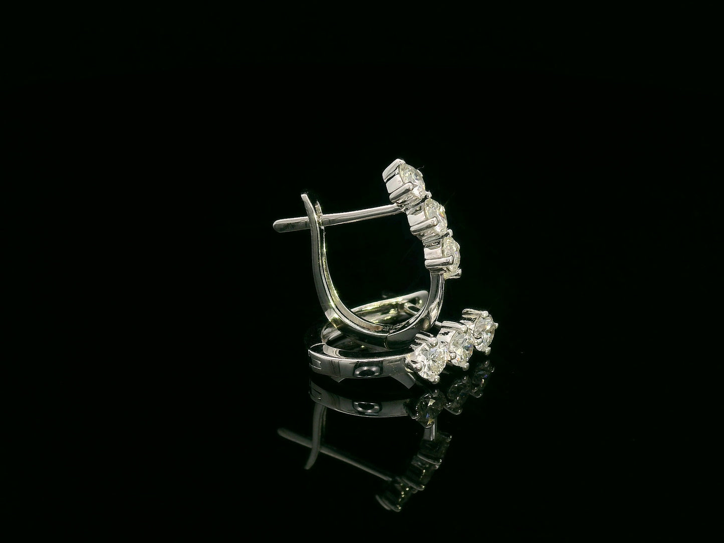18K white gold huggie hoop earrings featuring three round brilliant-cut diamonds along the front, totaling 0.57 carat.