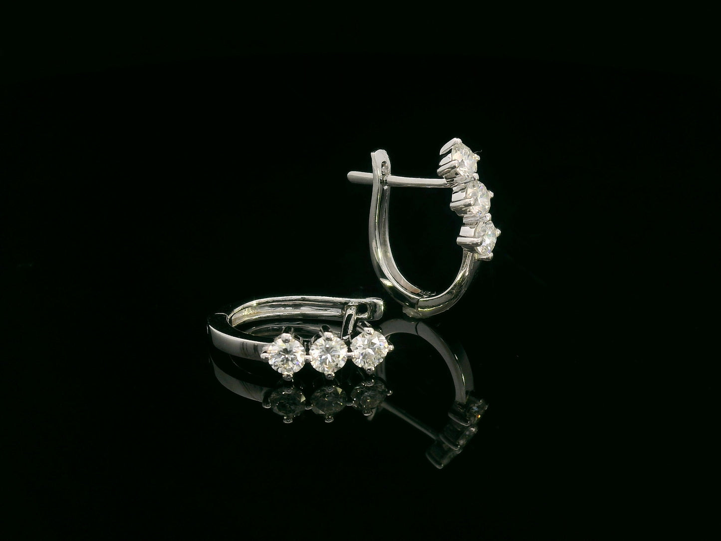 18K white gold huggie hoop earrings featuring three round brilliant-cut diamonds along the front, totaling 0.57 carat.