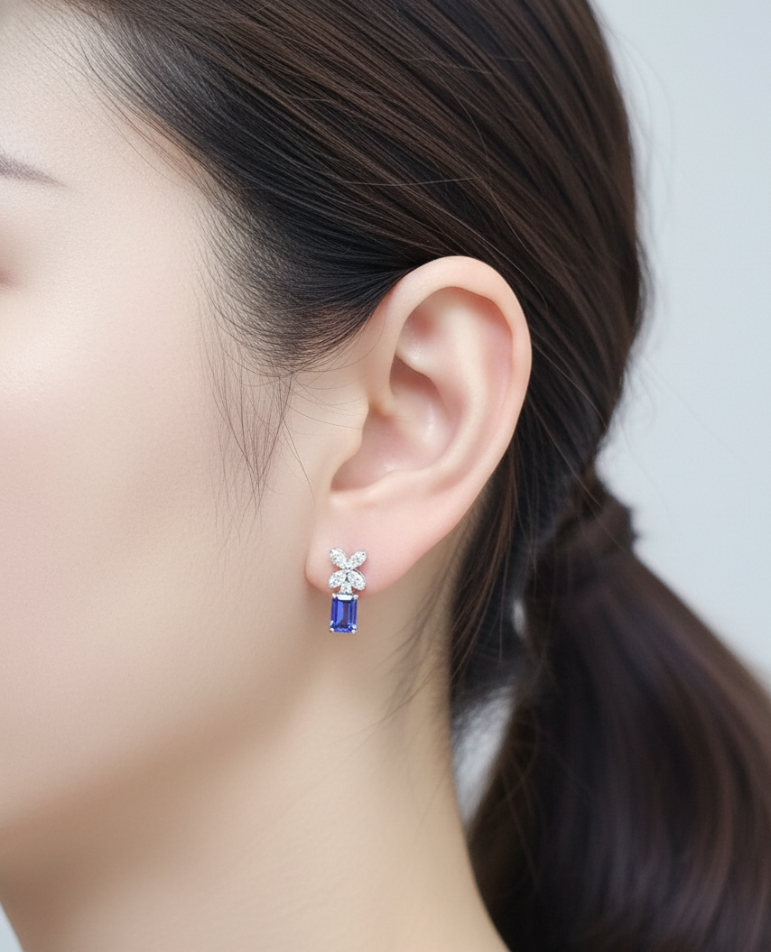 18K white gold earrings featuring emerald-cut Tanzanites beneath floral diamond clusters, total 1.56 carat