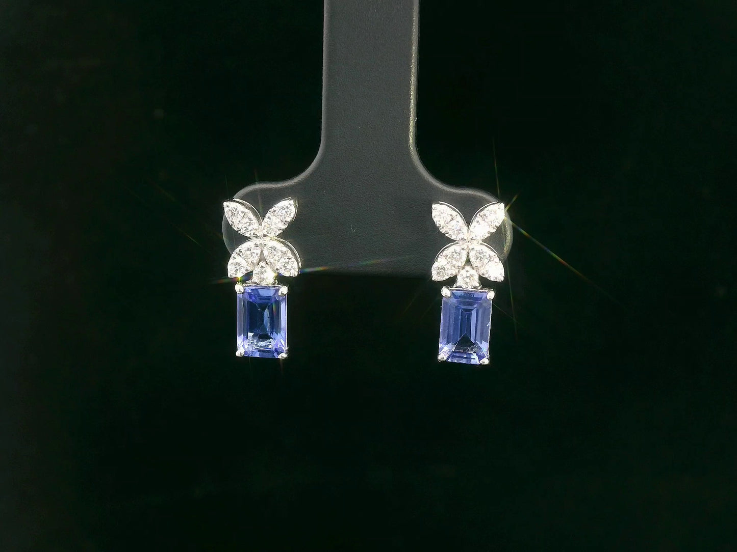 18K white gold earrings featuring emerald-cut Tanzanites beneath floral diamond clusters, total 1.56 carat