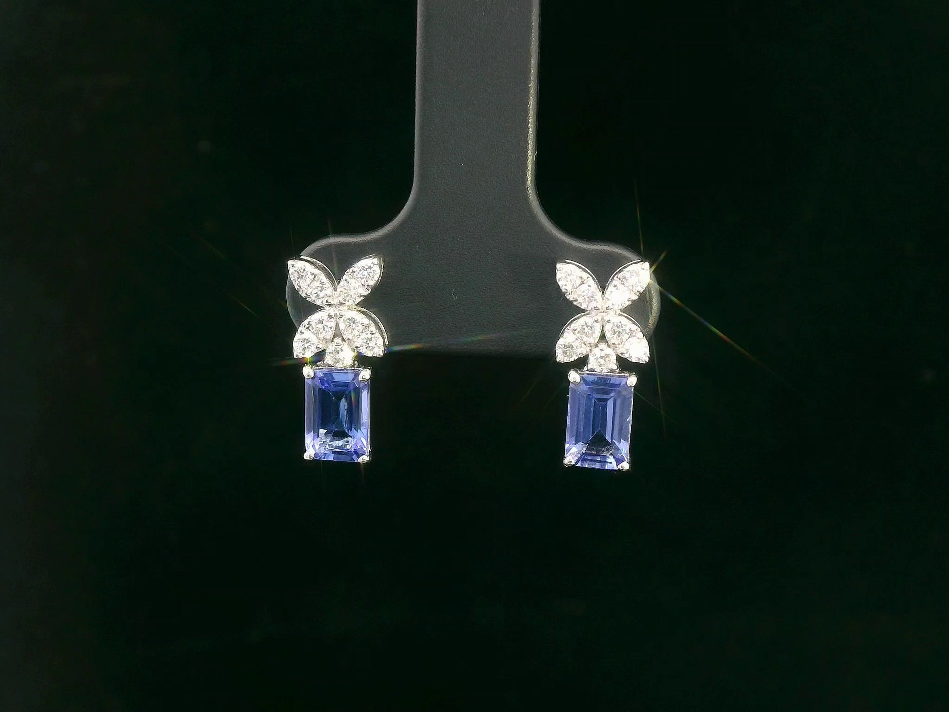 18K white gold earrings featuring emerald-cut Tanzanites beneath floral diamond clusters, total 1.56 carat