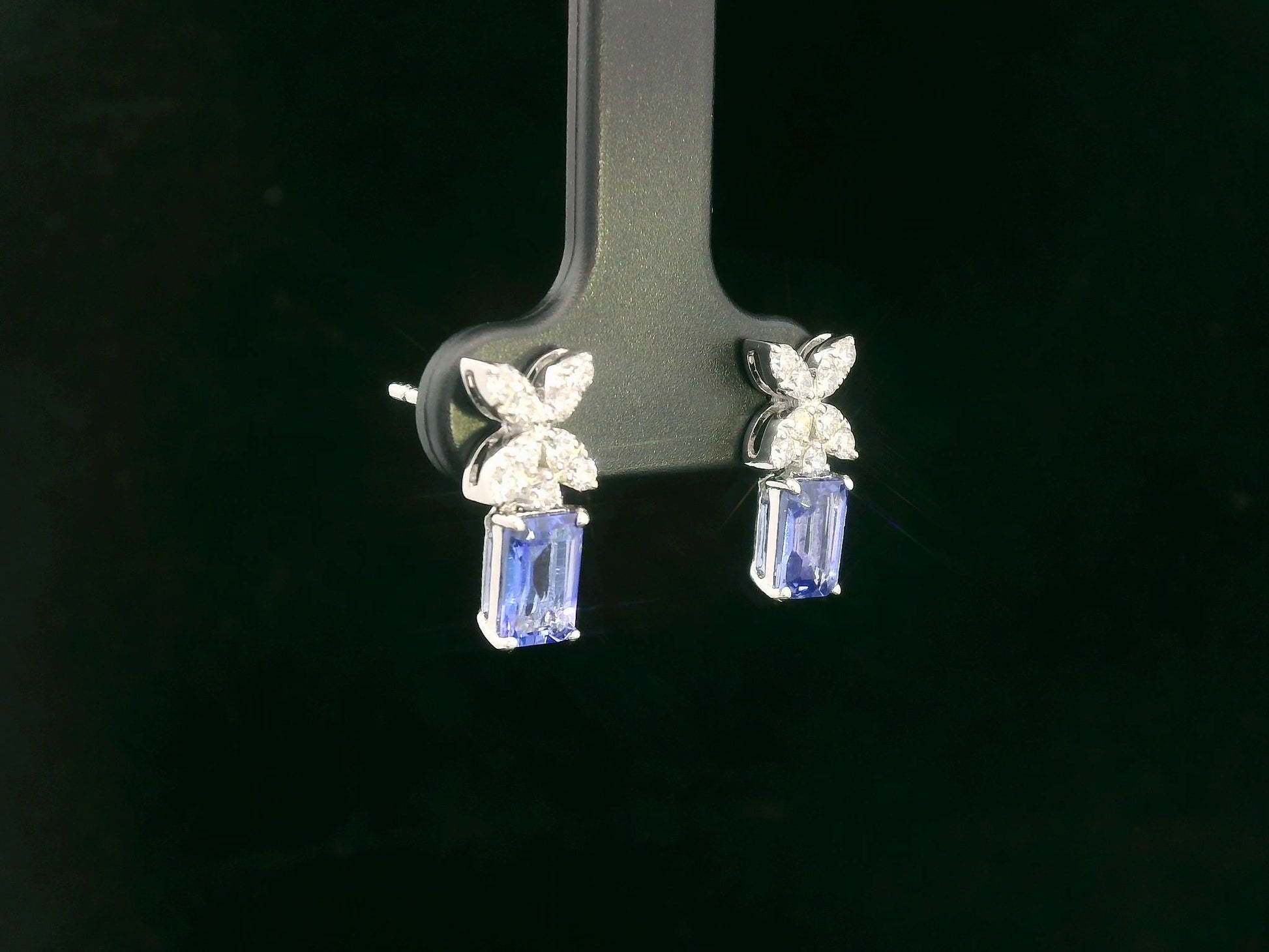 18K white gold earrings featuring emerald-cut Tanzanites beneath floral diamond clusters, total 1.56 carat