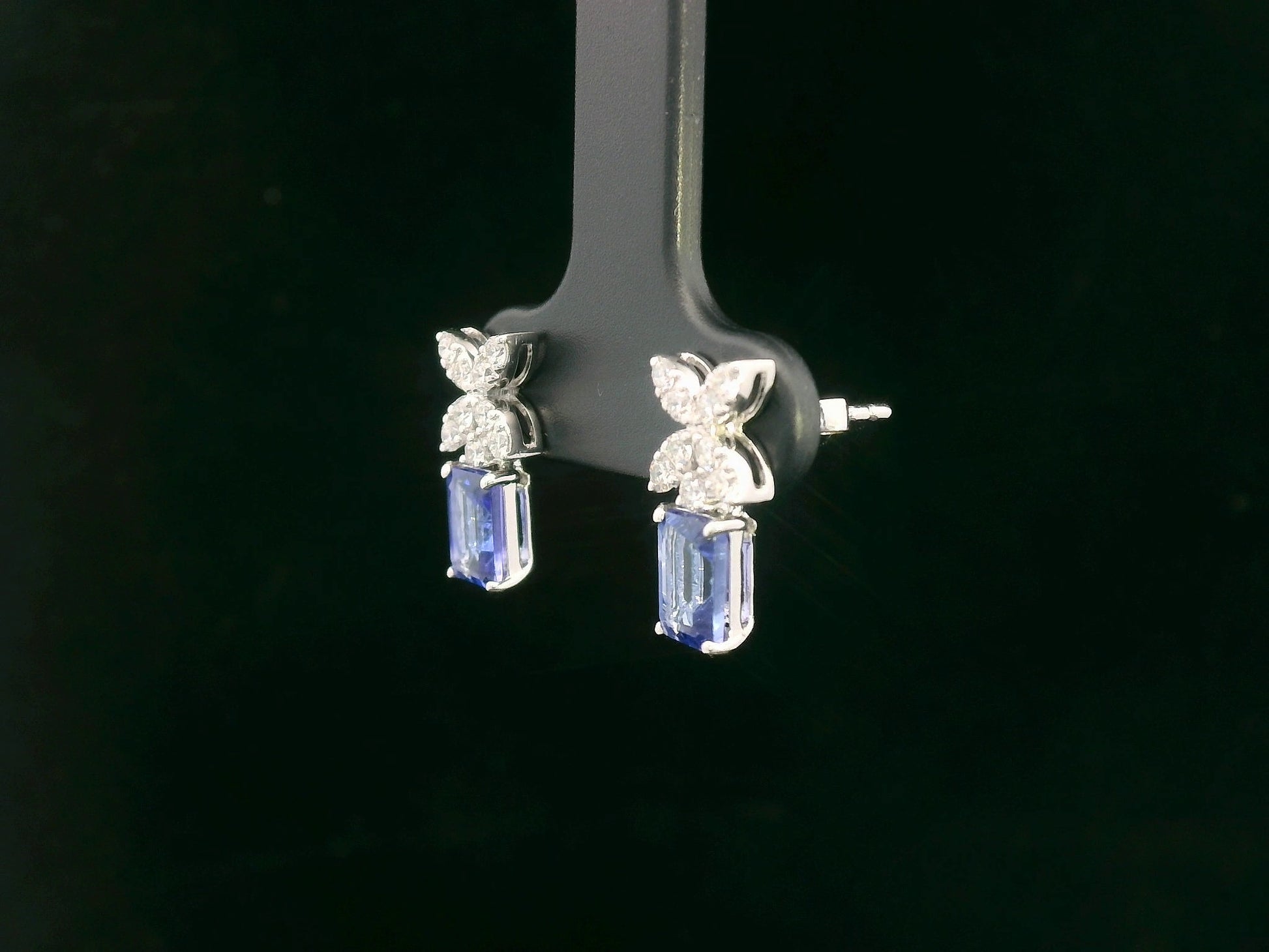 18K white gold earrings featuring emerald-cut Tanzanites beneath floral diamond clusters, total 1.56 carat