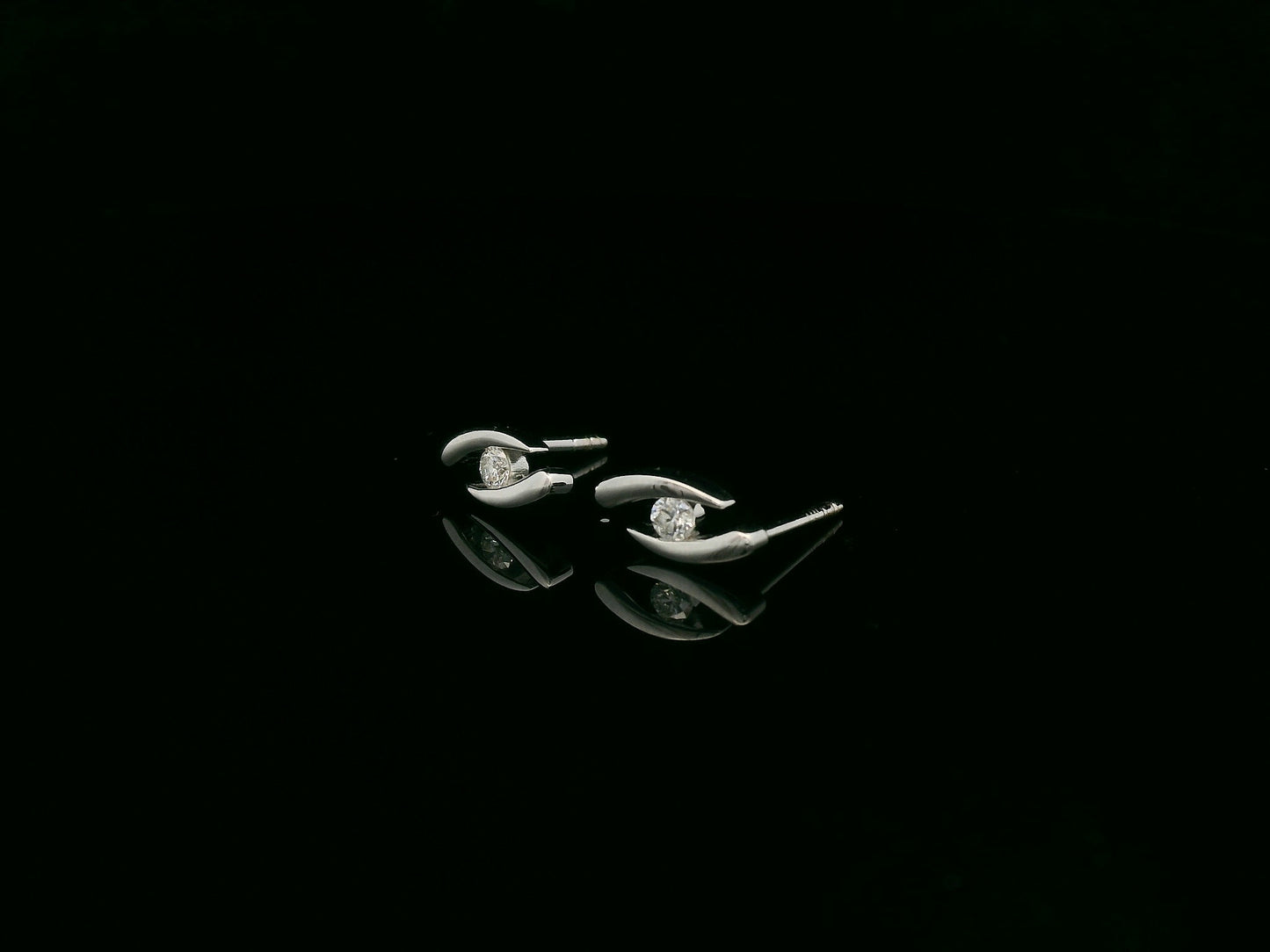 18K white gold modern diamond stud earrings with sculptural swirl design and round diamonds, total diamond weight 0.12 carat, Emirates Diamonds.