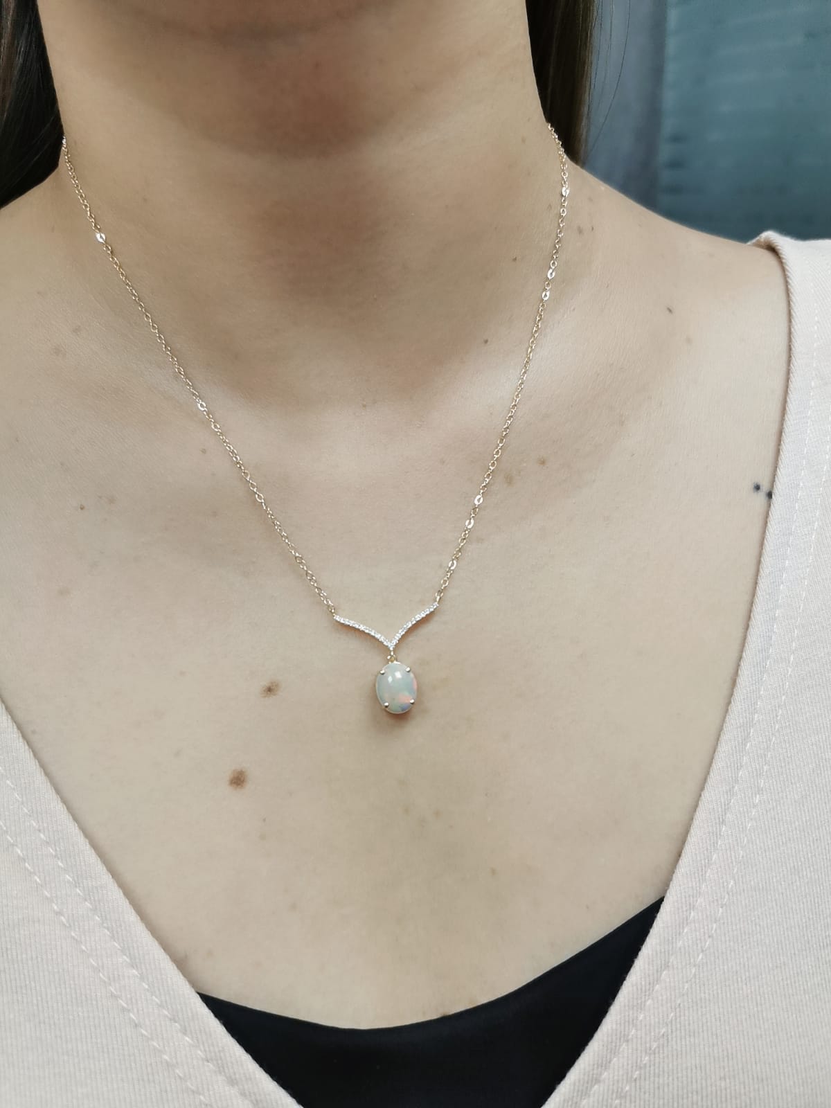 18K gold necklace with a 1.30-carat oval opal pendant, accented by a V-shaped row of pave-set diamonds totaling 0.10 carats, suspended on a delicate gold chain.