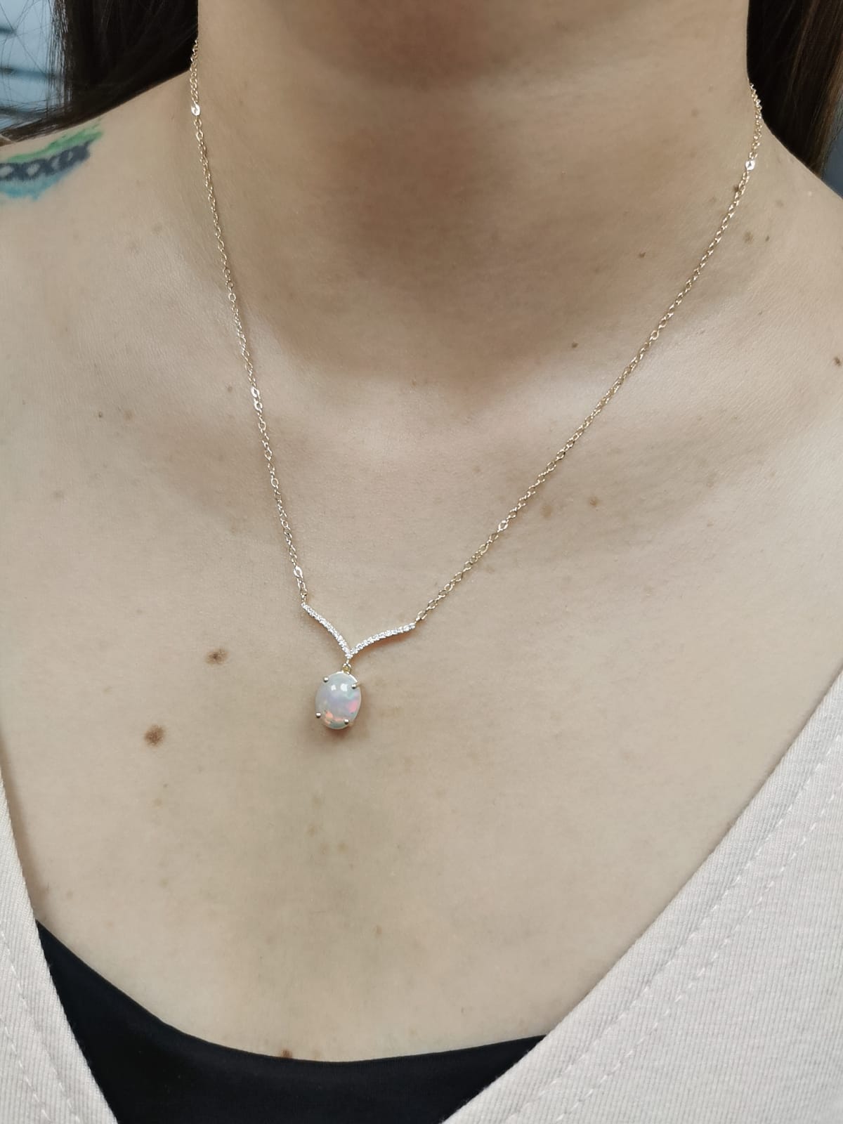 18K gold necklace with a 1.30-carat oval opal pendant, accented by a V-shaped row of pave-set diamonds totaling 0.10 carats, suspended on a delicate gold chain.