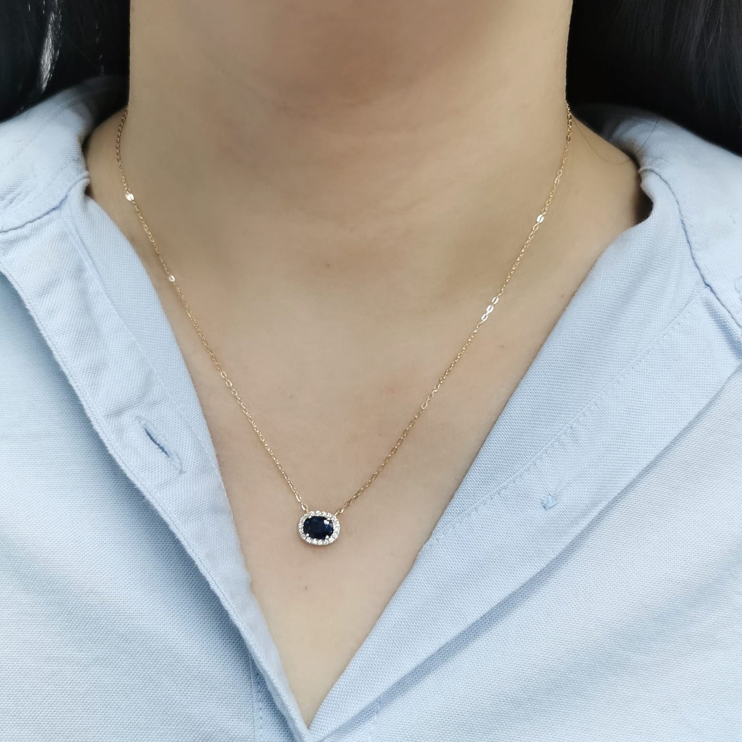 18K gold necklace featuring a 1.19-carat oval Blue Sapphire pendant, surrounded by a 0.14-carat diamond halo, suspended from a fine gold chain. Ideal for layering.