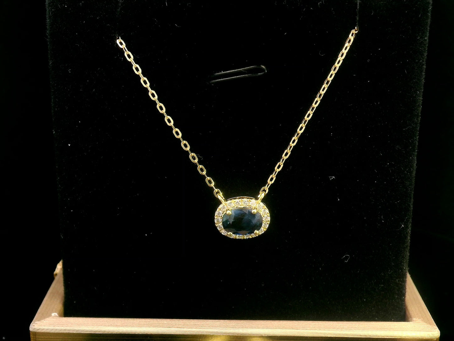 18K gold necklace featuring a 1.19-carat oval Blue Sapphire pendant, surrounded by a 0.14-carat diamond halo, suspended from a fine gold chain. Ideal for layering.
