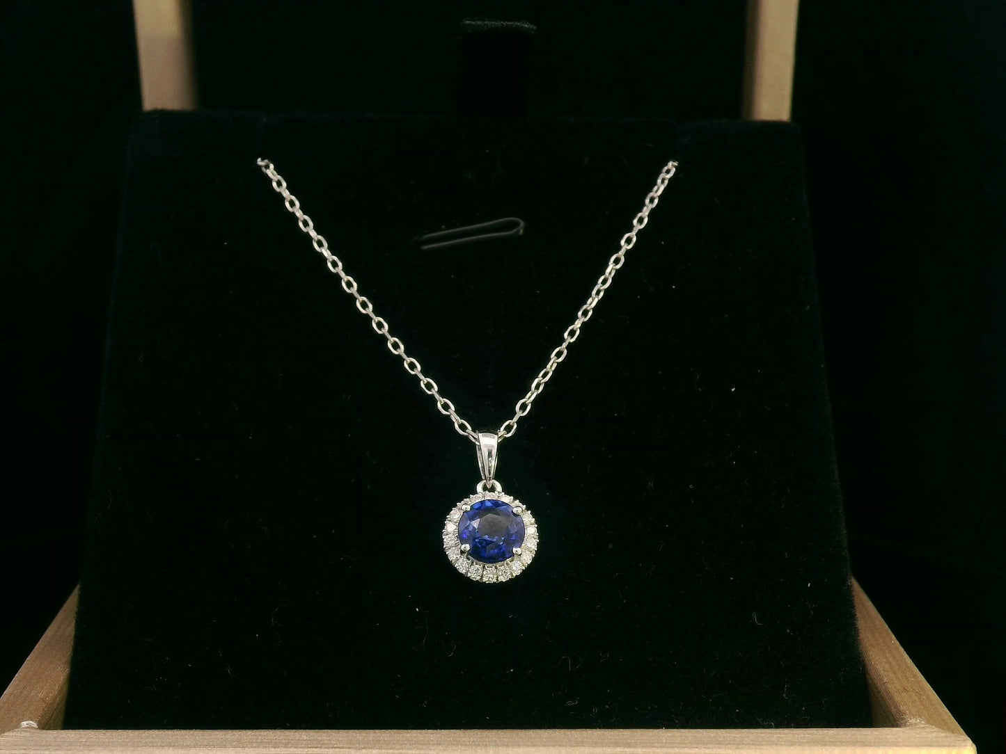 "18K white gold sapphire and diamond halo pendant featuring a 0.72ct deep blue sapphire surrounded by a 0.10ct diamond halo,