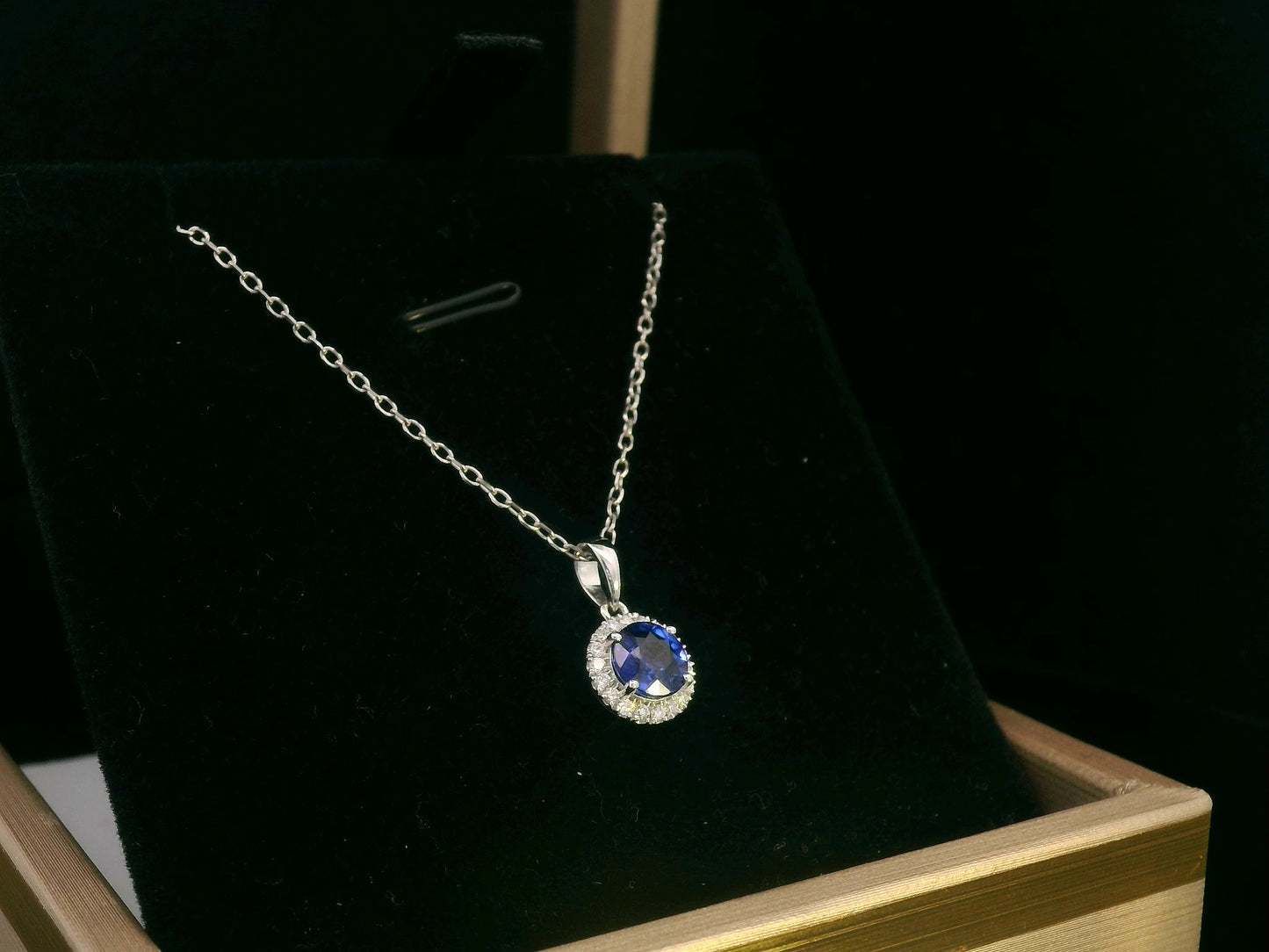 "18K white gold sapphire and diamond halo pendant featuring a 0.72ct deep blue sapphire surrounded by a 0.10ct diamond halo,