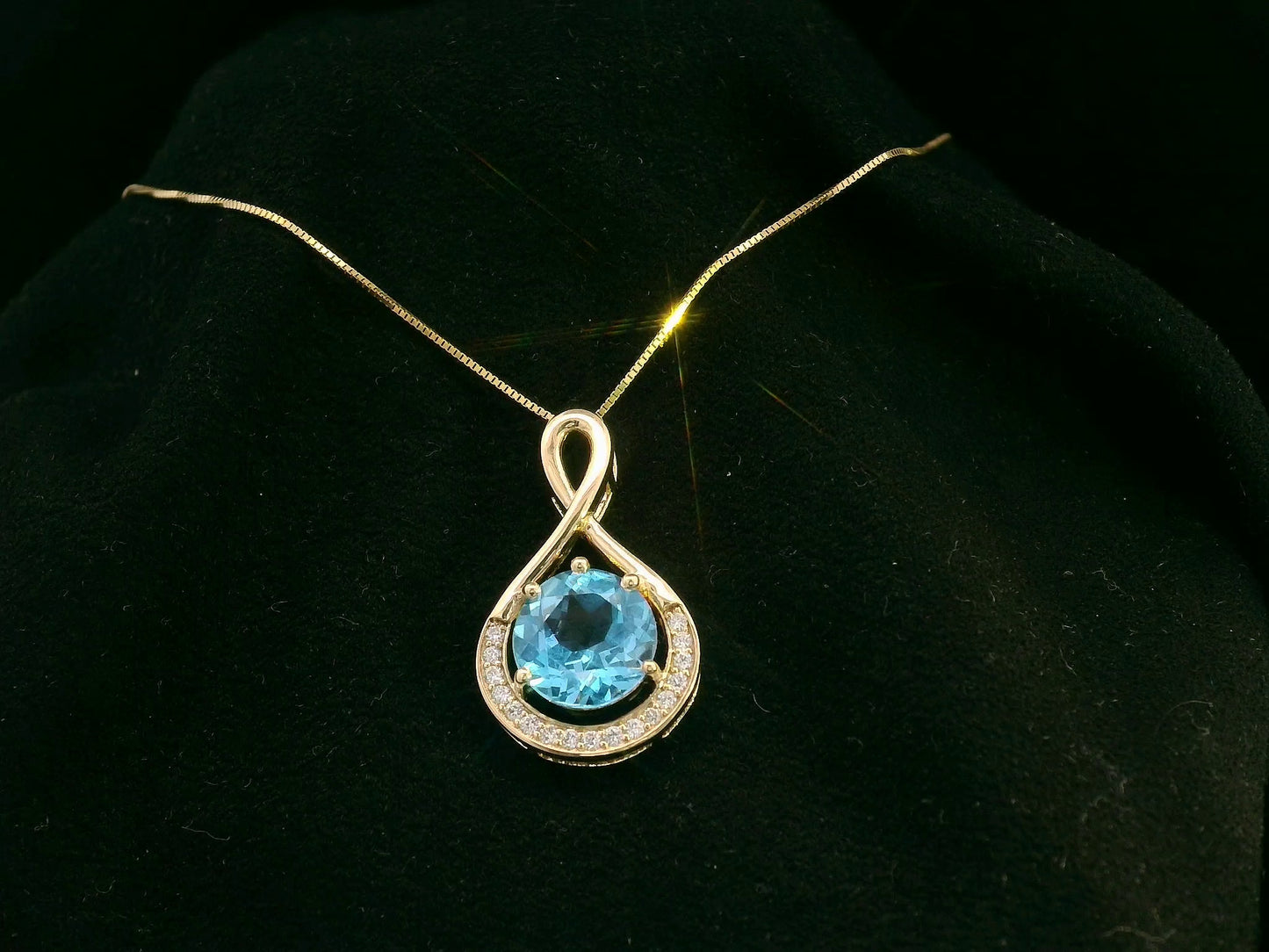 18k yellow gold pendant with 2.30 carat Swiss blue topaz center, diamond halo, and infinity-style bale