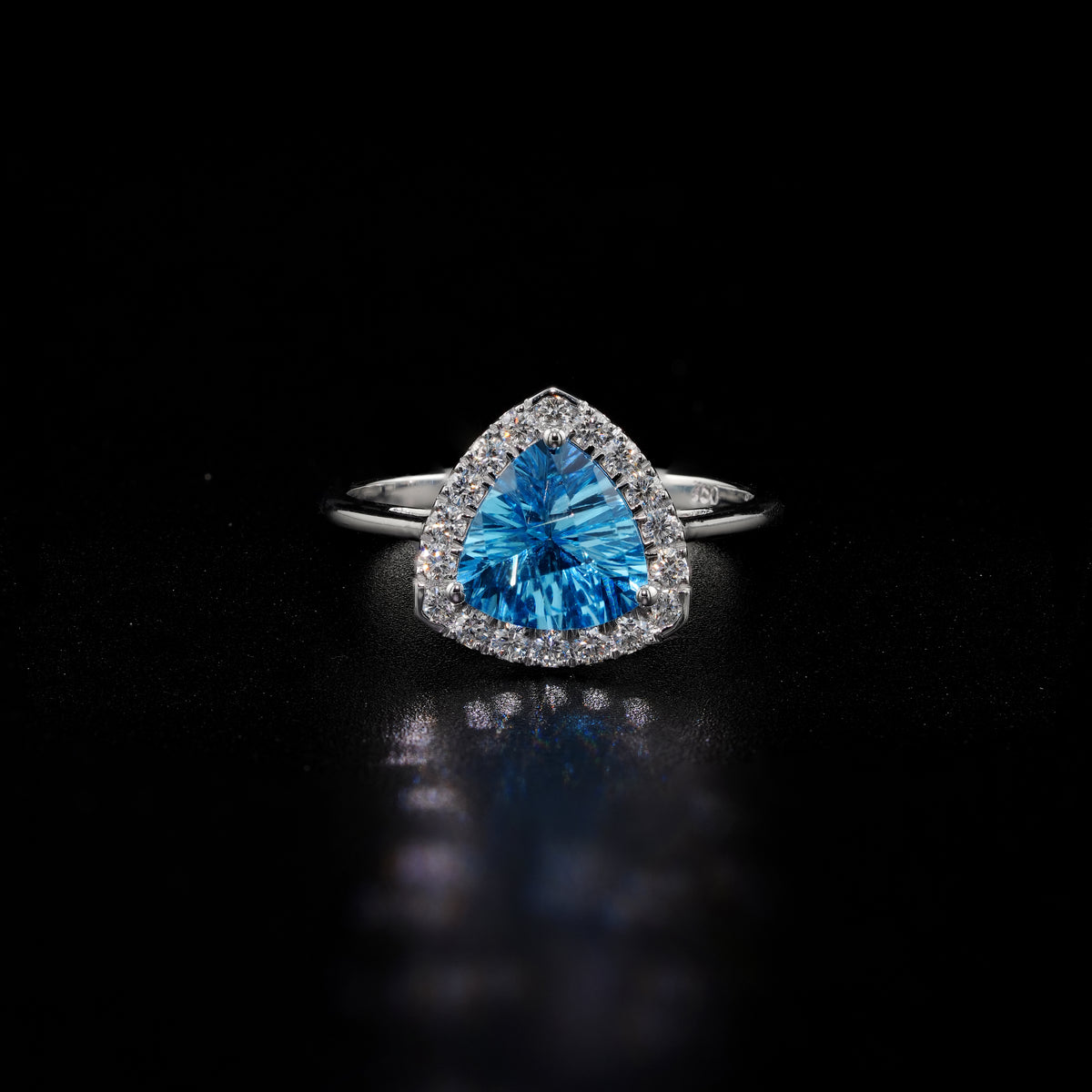 18K white gold ring with a triangular bright blue topaz surrounded by round diamonds and polished split-shank shoulders.