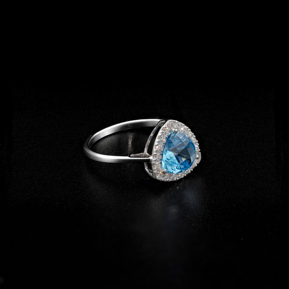 18K white gold ring with a triangular bright blue topaz surrounded by round diamonds and polished split-shank shoulders.