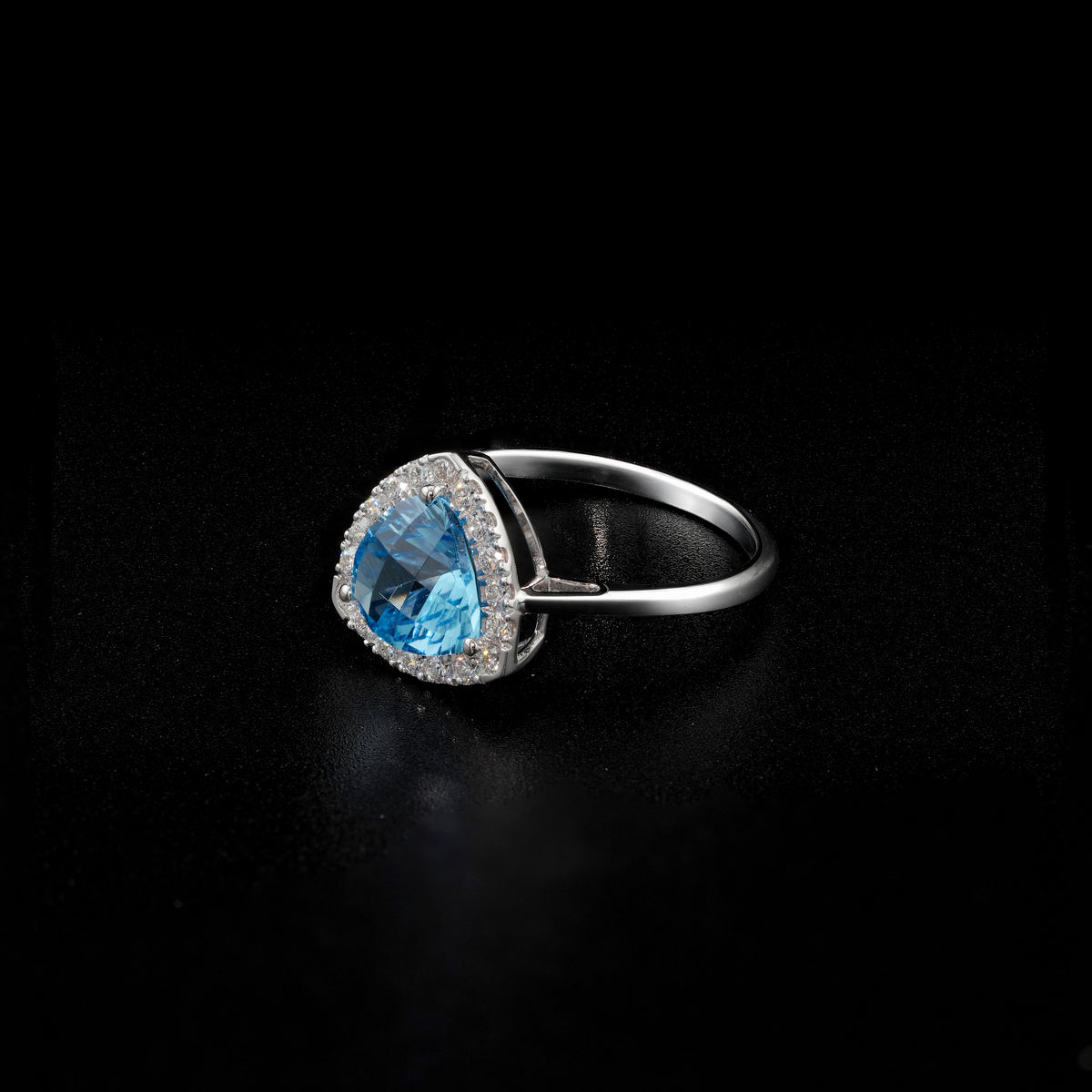 18K white gold ring with a triangular bright blue topaz surrounded by round diamonds and polished split-shank shoulders.