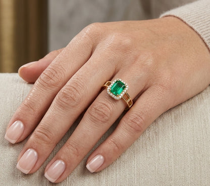 Emerald and diamond halo ring in 18K yellow gold featuring a rectangular green emerald and geometric openwork band.
