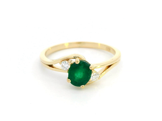 18K yellow gold ring featuring a 0.75-carat round-cut emerald with 0.10-carat diamond accents on a split-shank band – fine jewelry.