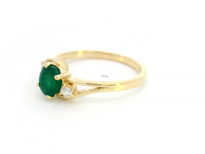 18K yellow gold ring featuring a 0.75-carat round-cut emerald with 0.10-carat diamond accents on a split-shank band – fine jewelry.