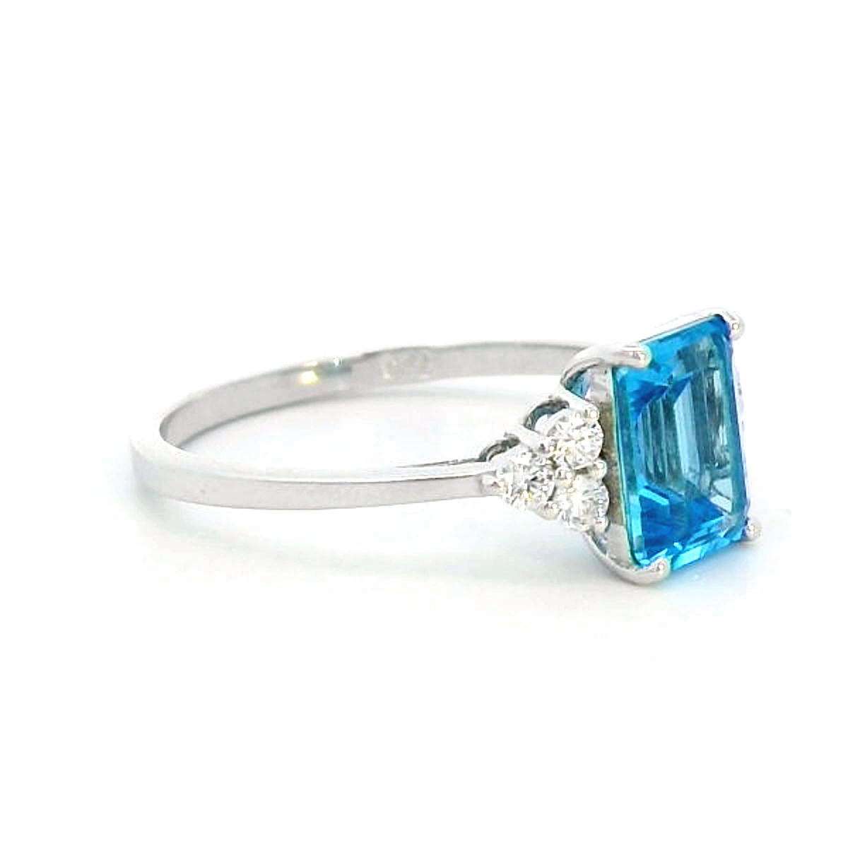 Elegant Swiss Blue Topaz and diamond ring in 18K gold, featuring a 1.66-carat emerald-cut Swiss Blue Topaz flanked by 0.17-carat diamonds in a classic three-stone design.