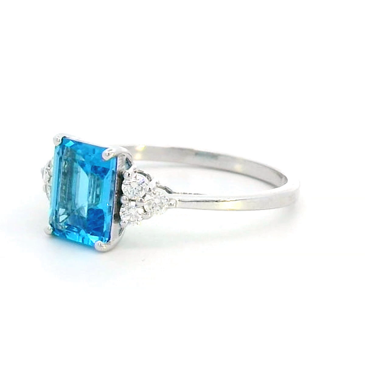 Elegant Swiss Blue Topaz and diamond ring in 18K gold, featuring a 1.66-carat emerald-cut Swiss Blue Topaz flanked by 0.17-carat diamonds in a classic three-stone design.