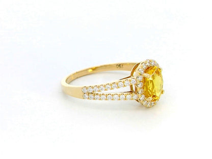 Yellow sapphire and diamond halo ring in 18K yellow gold featuring a 1.21-carat oval yellow sapphire, surrounded by a diamond halo and a split band adorned with diamonds, totaling 0.35 carats, with a smooth polished gold finish