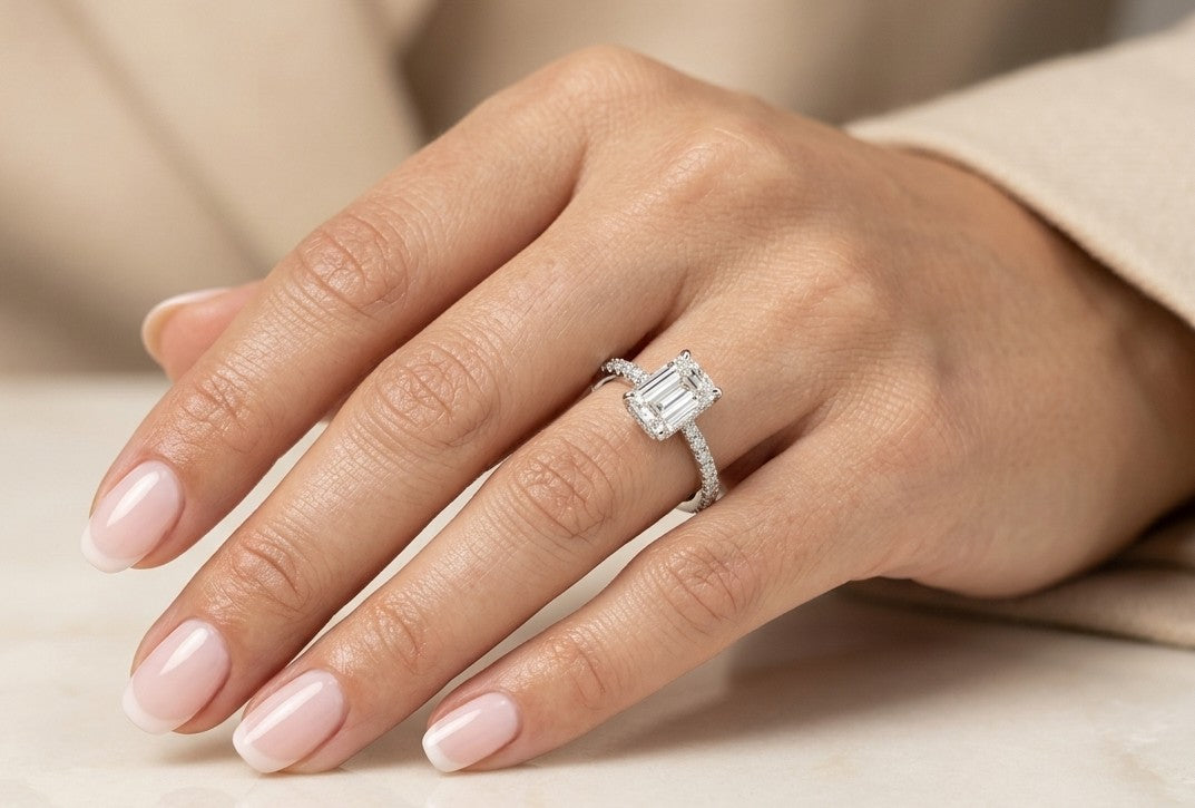 Emerald cut diamond engagement ring in 18K white gold with a four-prong centre setting and round diamonds along the band
