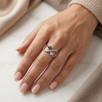 Blue sapphire and diamond infinity ring in 18K white gold with three round blue sapphires and diamond detailing.