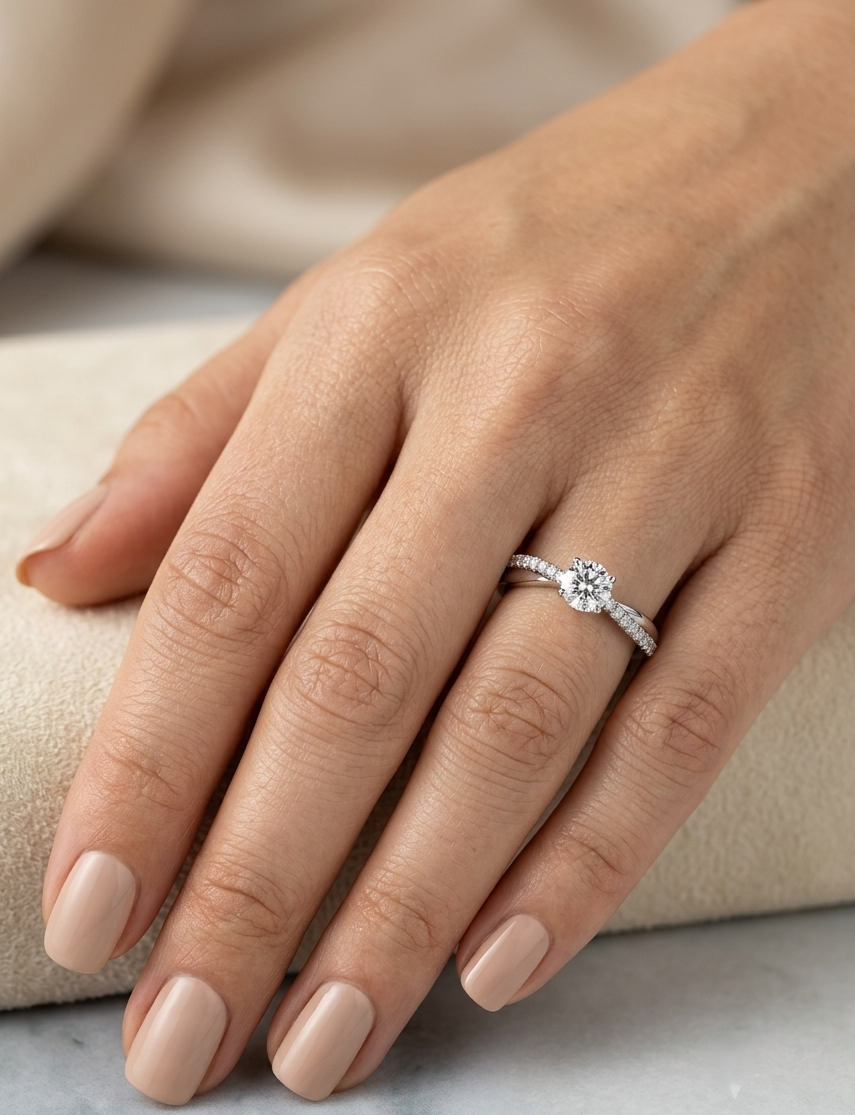 18K white gold minimalist engagement ring featuring a round brilliant diamond with an asymmetrical crossover band and pavé diamonds.