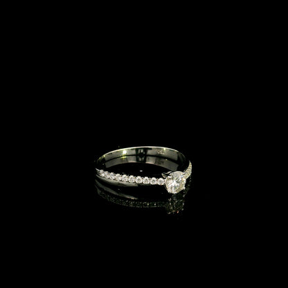 18K white gold minimalist engagement ring featuring a round brilliant diamond with an asymmetrical crossover band and pavé diamonds.