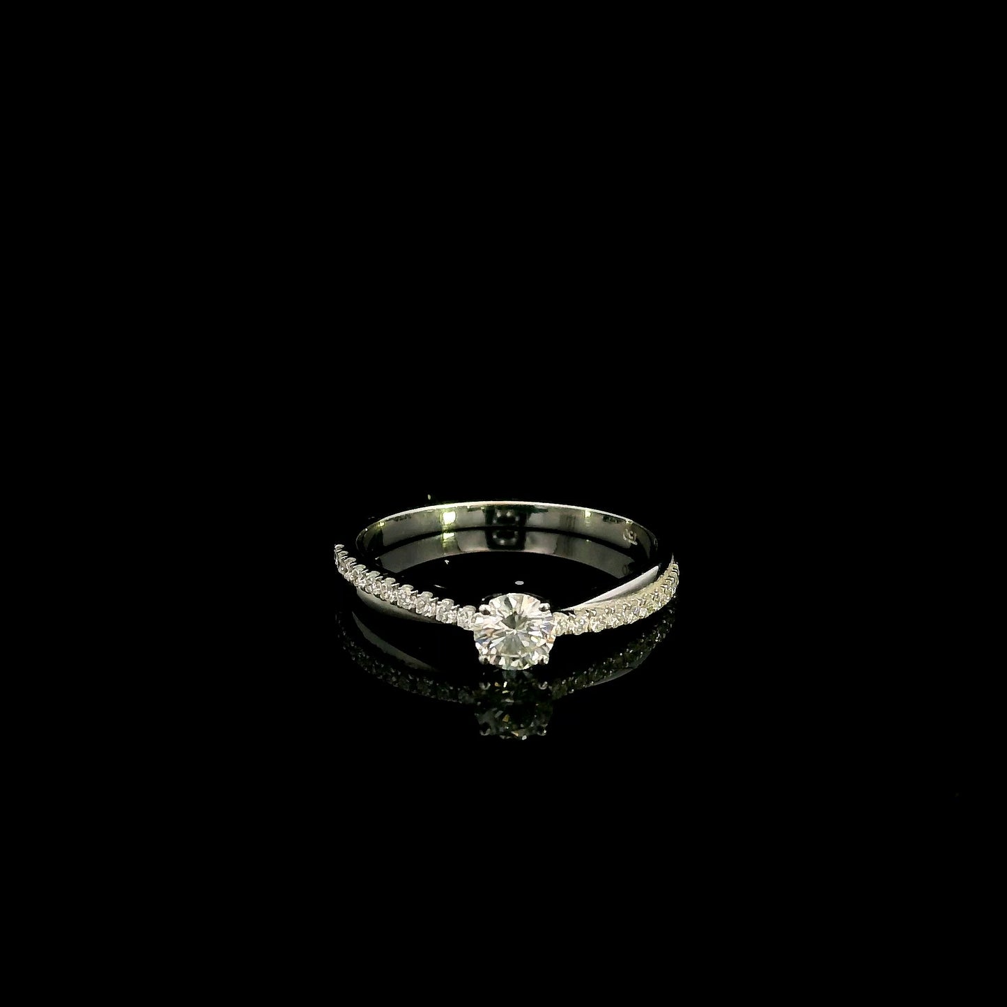 18K white gold minimalist engagement ring featuring a round brilliant diamond with an asymmetrical crossover band and pavé diamonds.