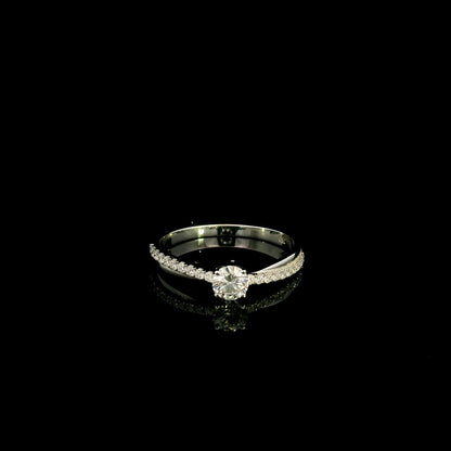 18K white gold minimalist engagement ring featuring a round brilliant diamond with an asymmetrical crossover band and pavé diamonds.