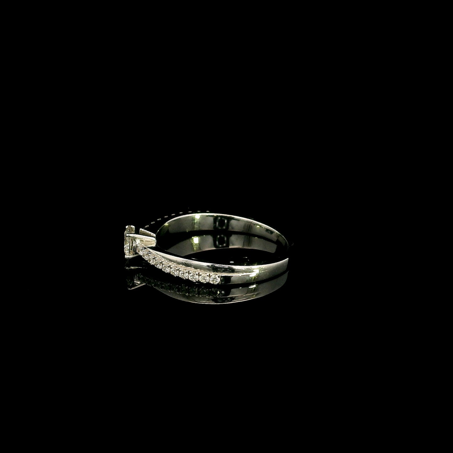 18K white gold minimalist engagement ring featuring a round brilliant diamond with an asymmetrical crossover band and pavé diamonds.