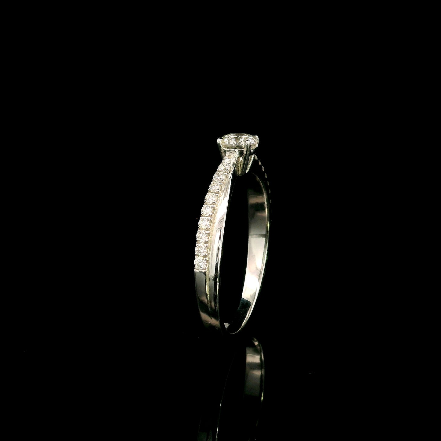 18K white gold minimalist engagement ring featuring a round brilliant diamond with an asymmetrical crossover band and pavé diamonds.