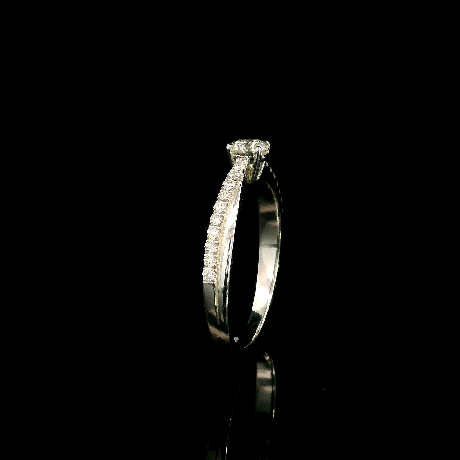 18K white gold minimalist engagement ring featuring a round brilliant diamond with an asymmetrical crossover band and pavé diamonds.