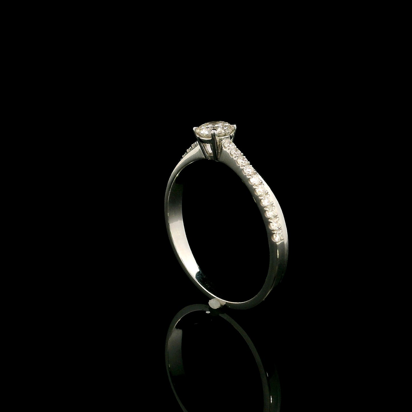 18K white gold minimalist engagement ring featuring a round brilliant diamond with an asymmetrical crossover band and pavé diamonds.