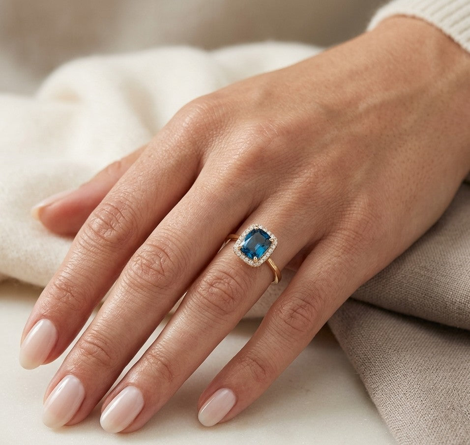 18K yellow gold ring with emerald cut London Blue Topaz surrounded by a round diamond halo