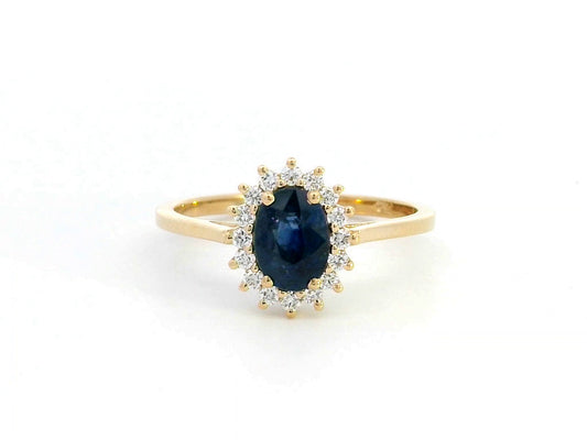 Oval Blue Sapphire and diamond halo ring in 18K gold, featuring a 1.02ct royal blue gemstone surrounded by 0.19ct round diamonds. Elegant fine jewelry inspired by Princess Diana’s iconic ring.