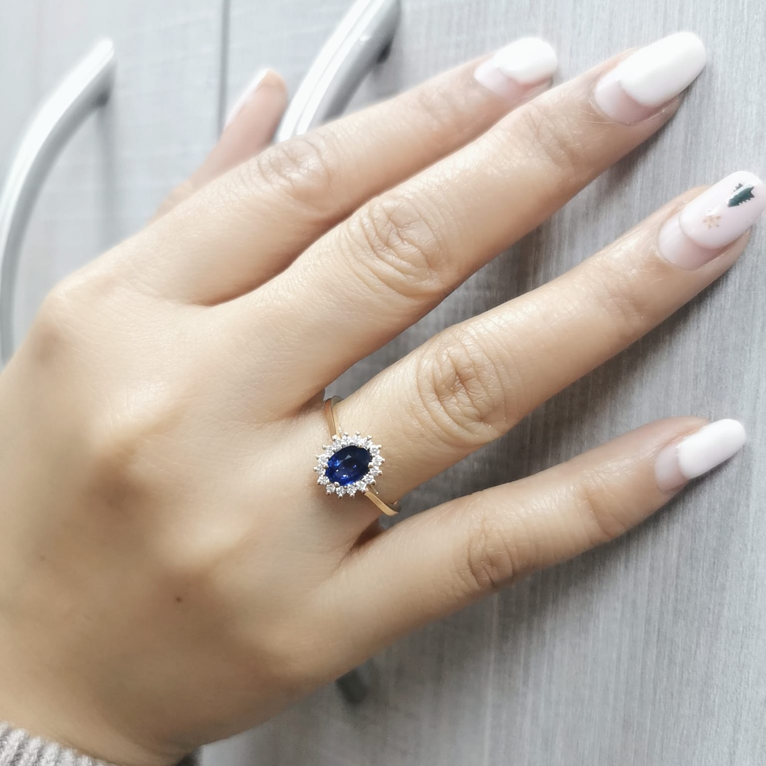 Oval Blue Sapphire and diamond halo ring in 18K gold, featuring a 1.02ct royal blue gemstone surrounded by 0.19ct round diamonds. Elegant fine jewelry inspired by Princess Diana’s iconic ring.