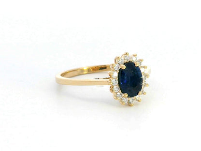 Oval Blue Sapphire and diamond halo ring in 18K gold, featuring a 1.02ct royal blue gemstone surrounded by 0.19ct round diamonds. Elegant fine jewelry inspired by Princess Diana’s iconic ring.