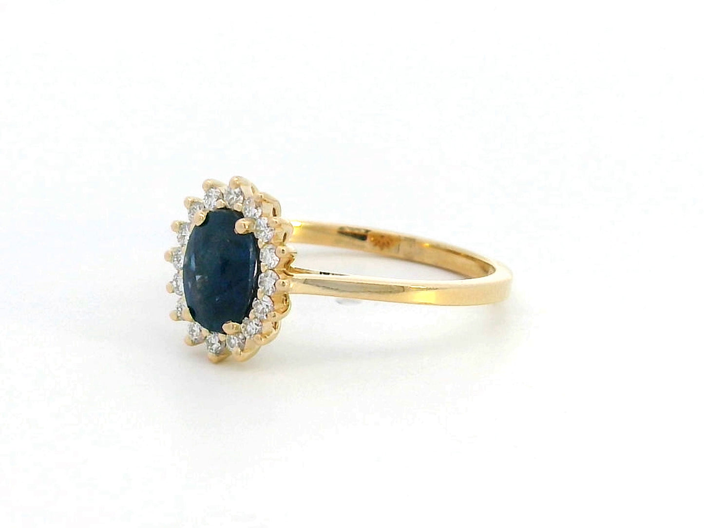 Oval Blue Sapphire and diamond halo ring in 18K gold, featuring a 1.02ct royal blue gemstone surrounded by 0.19ct round diamonds. Elegant fine jewelry inspired by Princess Diana’s iconic ring.