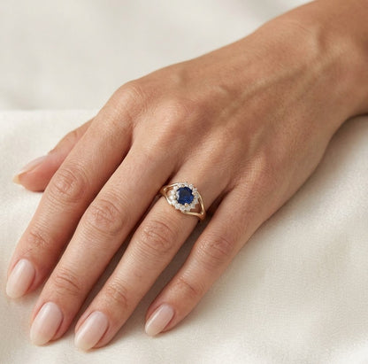 Round blue sapphire and diamond halo ring in 18K yellow gold with distinctive open gold shoulders.