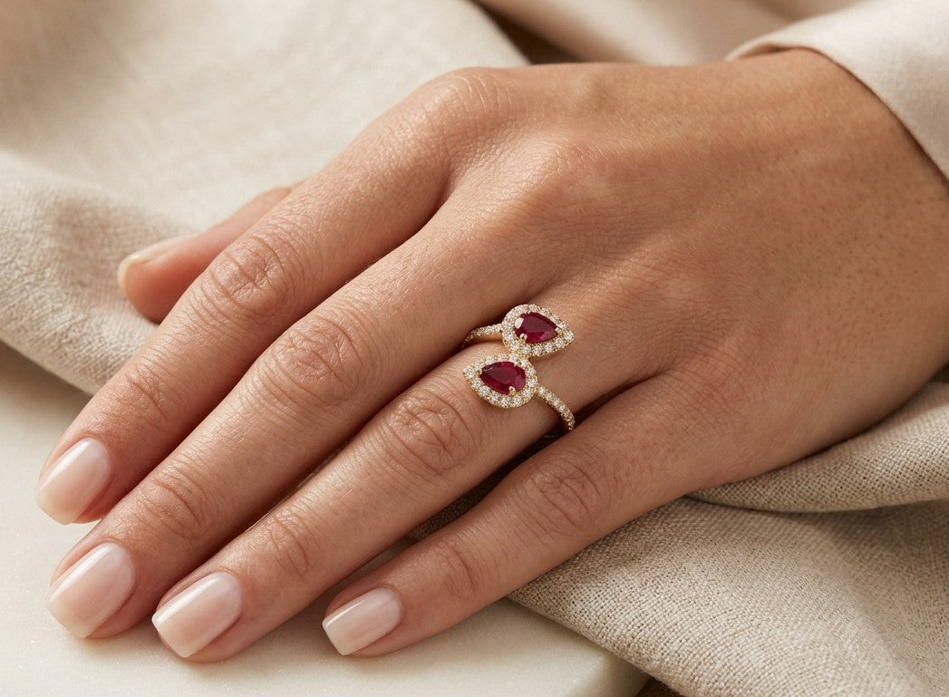 Two pear-shaped ruby and diamond halo ring in 18K yellow gold with an open two-stone design.