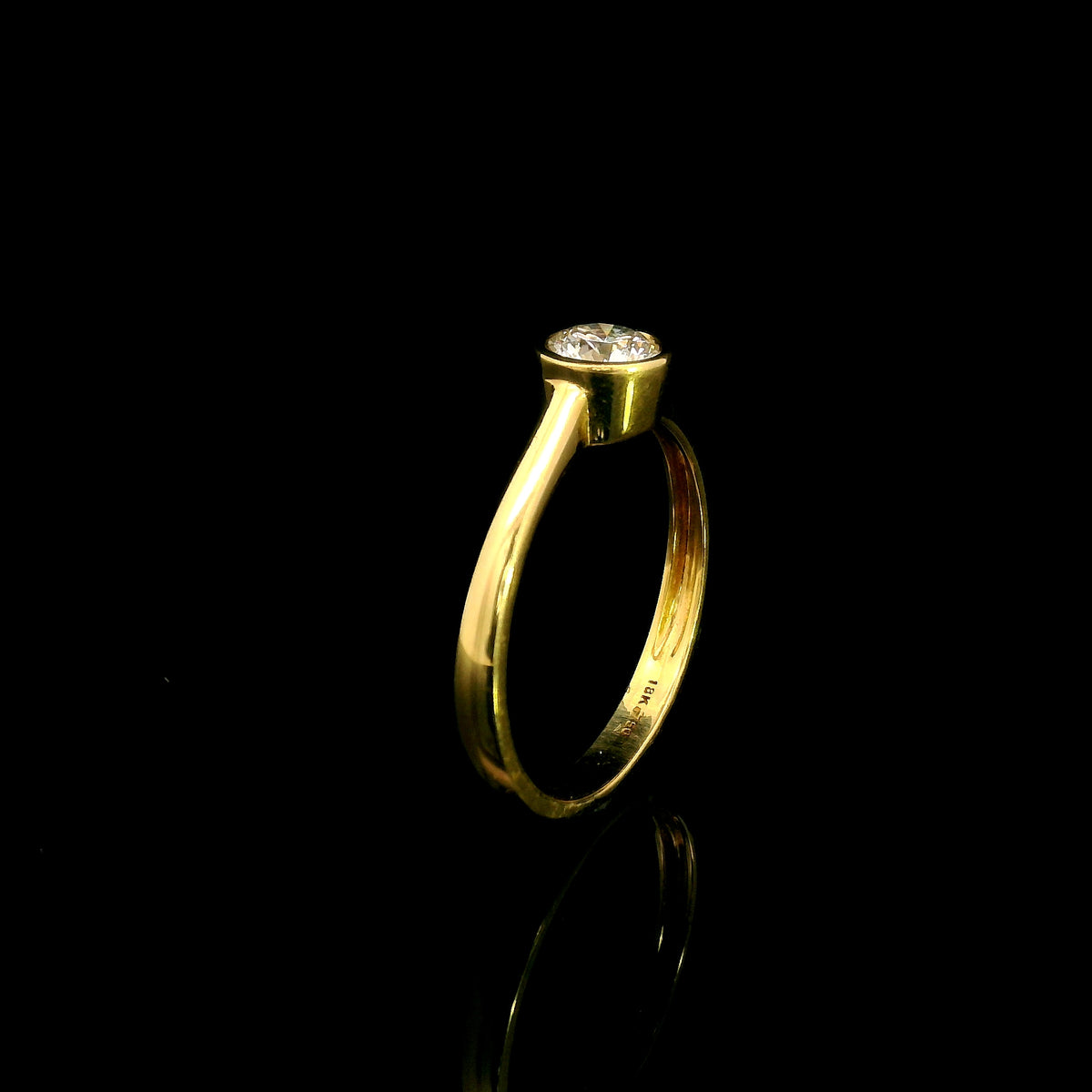 Round brilliant bezel set diamond engagement ring in 18K yellow gold with a slender solitaire band.