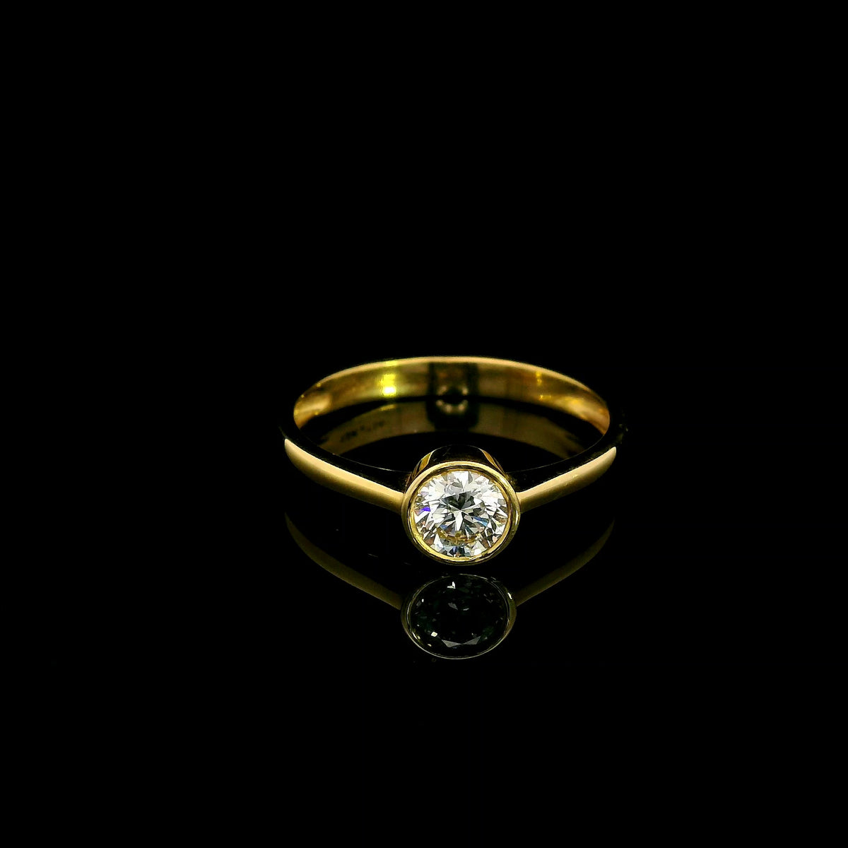 Round brilliant bezel set diamond engagement ring in 18K yellow gold with a slender solitaire band.