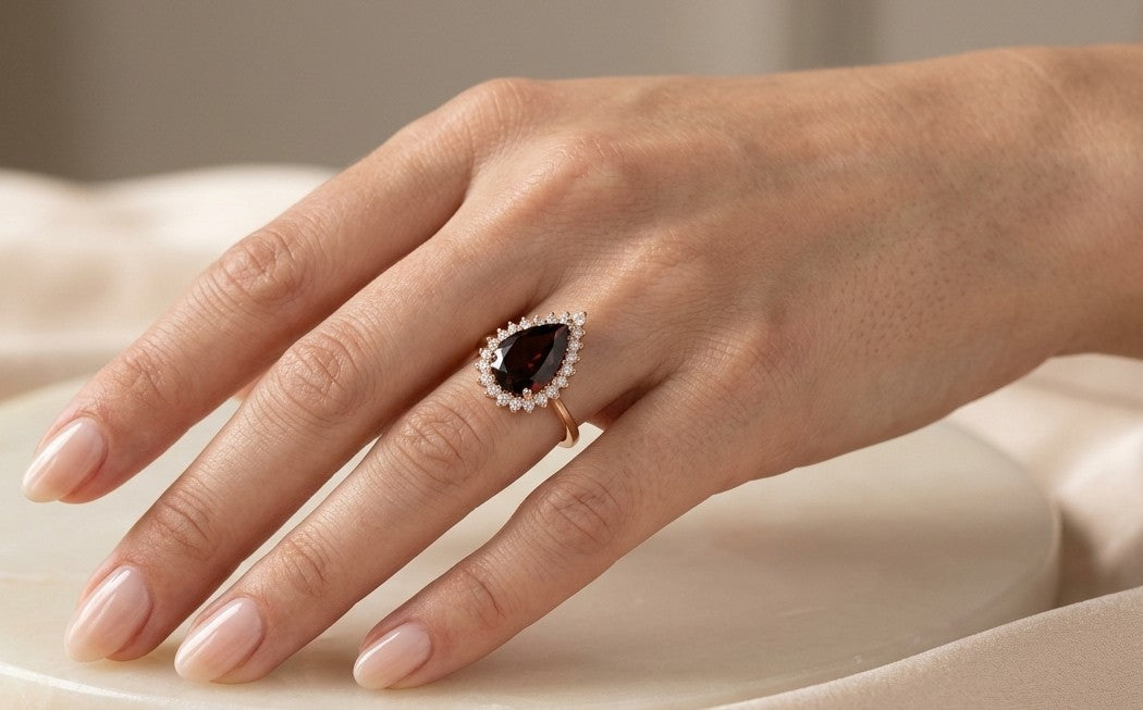 Garnet and diamond ring in 18K rose gold featuring a pear-shaped deep red garnet surrounded by graduated round brilliant diamonds.