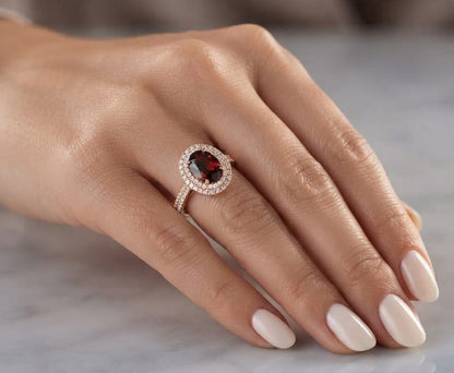Oval garnet and diamond double halo ring in 18K rose gold with diamond-set shoulders.